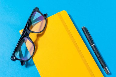 Sarı defter, mavi arka plan üzerinde gözlük.