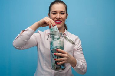 Genç ve çekici bir kadın elinde para dolu bir kavanoz tutuyor.