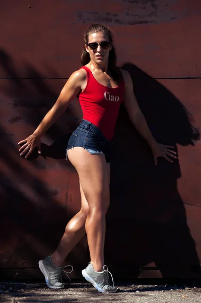 Hot sexy fitness vrouw dragen rode badpak en jeans shorts. — Stockfoto