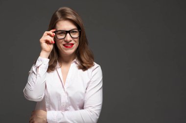 Gri arka planda gözlük takan mutlu, gülümseyen genç kadın..