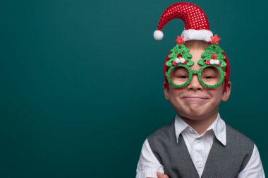 Noel Baba şapkalı küçük mutlu çocuk portresi ve Noel ağaçlı komik gözlükler.