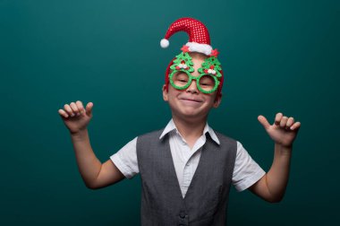 Noel Baba şapkalı neşeli çocuk portresi ve Noel ağaçlı komik gözlükler.