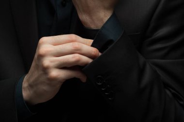 Koyu renk gömlekli ve ceketli tanımlanamayan genç adam takım elbisesini düzeltiyor..