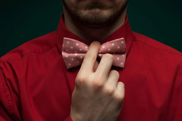Primer plano de las manos de un joven con una camisa roja que corrige la pajarita sobre un fondo verde. El concepto de galantería y estilo — Foto de Stock