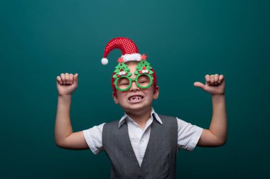 Noel Baba şapkalı neşeli çocuk portresi ve Noel ağaçlı komik gözlükler.