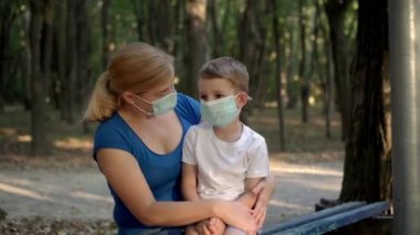 Tıp maskeli anne ve oğlu parkta oturuyor.