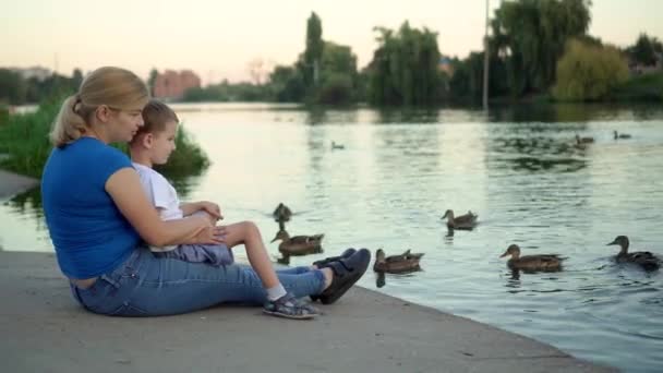 Madre e hijo en máscaras médicas alimentan patos en el lago — Vídeos de Stock