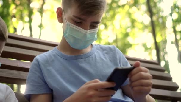 Les adolescents avec des masques médicaux jouent avec les smartphones dans le parc — Video