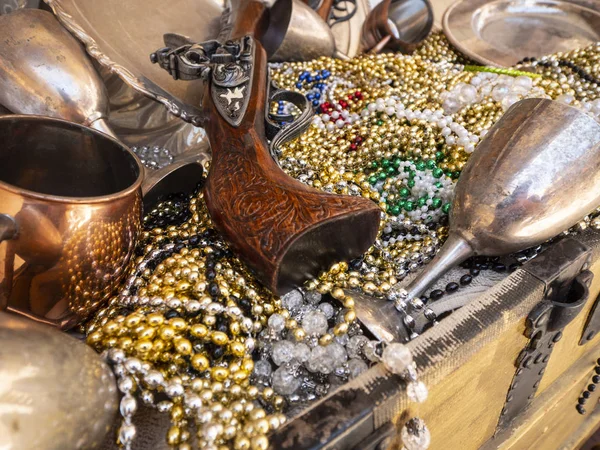A close up image of pirates chest treasures including, bead necklaces, guns and dinnerware.