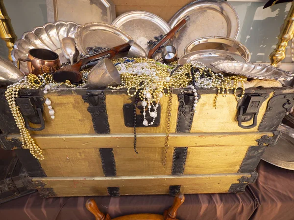 A close up image of pirates chest treasures including, bead necklaces, guns and dinnerware.