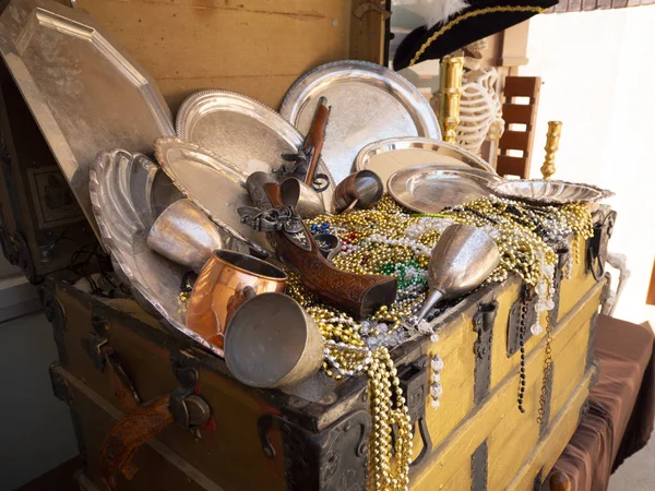 A close up image of pirates chest treasures including, bead necklaces, guns and dinnerware.