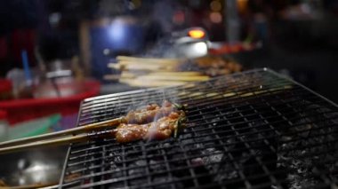 Sokak gıda satıcı hazırlar ve satan ızgara domuz eti, sopa üzerinde Barbekü domuz eti gece Pazarı'na, kızarmış. Closeup.4K