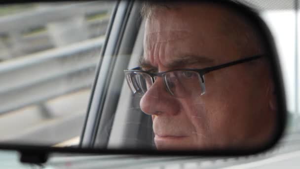 年配の男性は、国の道路で車を運転します。自動車のバックミラーに顔を映し出す。クローズ アップ。4 k — ストック動画