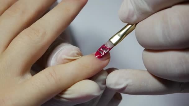 La manicurista de primer plano aplica un esmalte de uñas en gel rojo. Mujer en salón de spa de belleza haciendo manicura — Vídeos de Stock