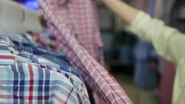 Vista lateral de la mano de la joven mujer eligiendo camisas en la tienda — Vídeo de stock