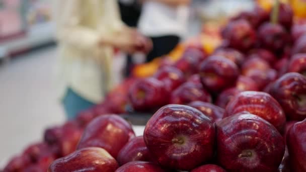 В супермаркете много яблок. Женщина выбирает фрукты во время покупок — стоковое видео