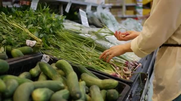 Las manos femeninas eligen la hoja de cebolla en el supermercado. Mujer joven comprando comida saludable en el fondo borroso de una tienda — Vídeo de stock