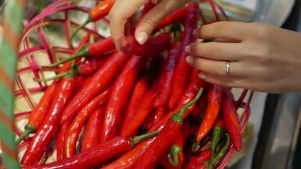 Ženská ruka výběrem a drží červené chilli papričky v úložišti. Mladá žena nákup zdravých potravin v rozostření pozadí supermarket — Stock video