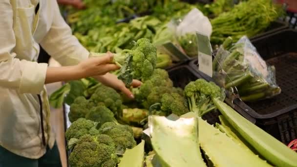 Elegir la mano femenina y comprar brócoli en una tienda. Mujer joven comprando alimentos saludables en el fondo borroso de un supermercado — Vídeo de stock