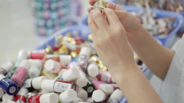 La mano de la mujer elegir y comprar un esmalte de uñas en un salón de belleza. Una mujer sosteniendo cosméticos — Vídeo de stock