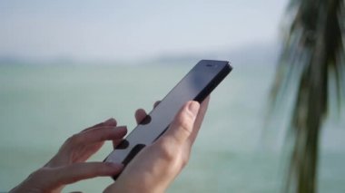 Arka plan deniz ve palmiye ağaçları üzerinden akıllı telefon kullanarak WOMANS eller. Kız dokunuşunda ekran