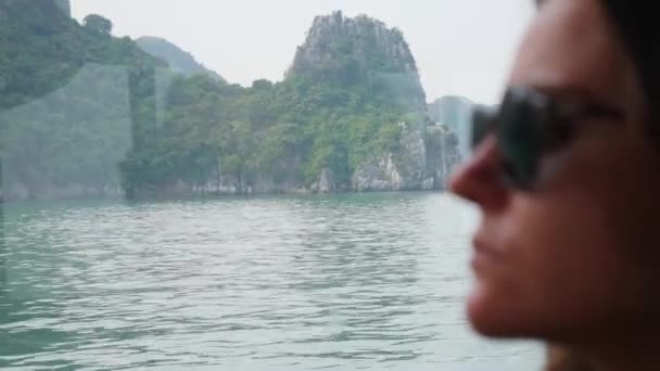 Uma jovem mulher sentada dentro de um barco com uma camisola branca e óculos de sol está olhando para a bela vista da baía. Conceito de viagem — Vídeo de Stock