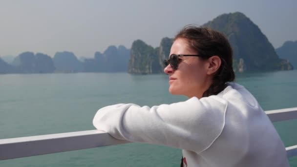 Mujer joven con una chaqueta blanca y gafas de sol están mirando a la hermosa vista de la bahía mientras está sentado en el barco. Concepto de viaje — Vídeos de Stock