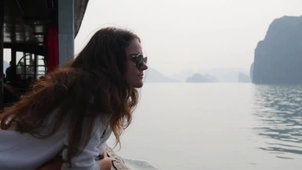 Mujer joven con una chaqueta blanca y gafas de sol están mirando a la hermosa vista de la bahía mientras está sentado en el barco. Concepto de viaje — Vídeos de Stock