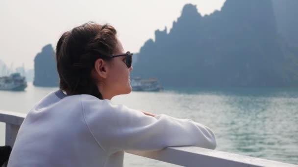 Mujer joven con una chaqueta blanca y gafas de sol están mirando a la hermosa vista de la bahía mientras está sentado en el barco. Concepto de viaje — Vídeos de Stock