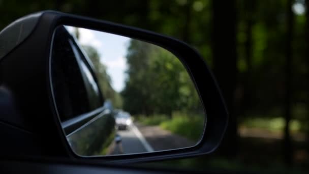 Смотрите в зеркало заднего вида, как автомобиль едет по проселочной дороге. 4K — стоковое видео