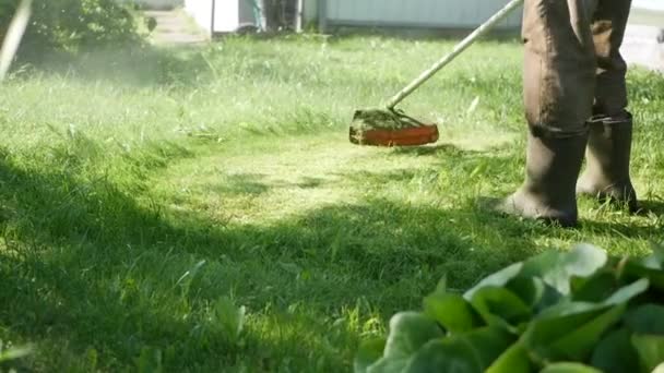 Arbeiter mit Benzin-Rasenmähertrimmer mit Motor beim Rasenmähen an einem sonnigen Sommertag. Rasenmähen auf dem Land. Zeitlupe — Stockvideo