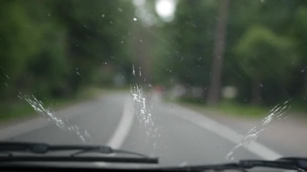 Los limpiaparabrisas limpian el parabrisas del coche sobre la marcha. Vista interior borrosa de un camino rural. 4k — Vídeo de stock