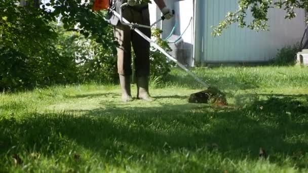 Travailleur masculin avec tondeuse à gazon à essence avec moteur coupant l'herbe par une journée d'été ensoleillée. Couper l'herbe dans le pays. Mouvement lent — Video