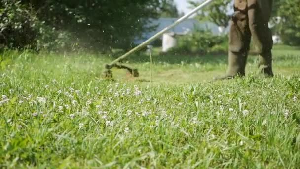 Мужчина с газонокосилкой и газонокосилкой с мотором, подстригающим траву в солнечный летний день. Кошение травы в деревне. Слоумоция — стоковое видео