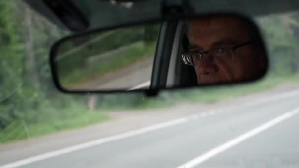 Starší muž jezdí autem po venkovské silnici. Odraz obličeje ve zpětném zrcátku auto. Detailní — Stock video