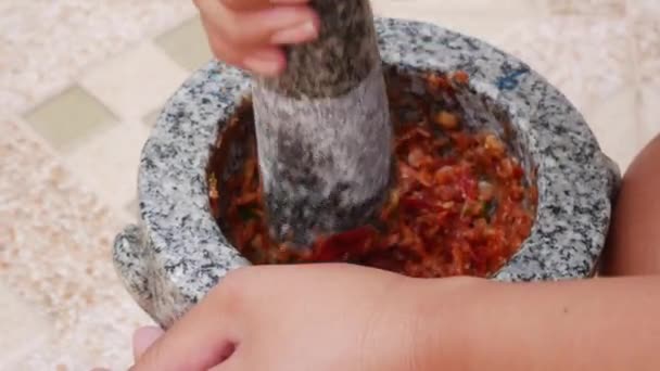 Chile tailandés y ajo machacando en mortero de piedra con mortero. Mujer preparando salsa para la sopa tailandesa tom yam. De cerca. 4k — Vídeo de stock