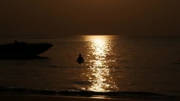 Silhouetten von Menschen, die am Strand spazieren und bei Sonnenuntergang im Meer schwimmen. Ferienkonzept. Nahaufnahme. 4k — Stockvideo