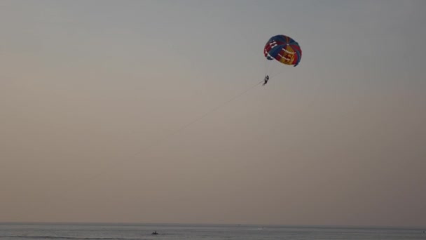 日没時の熱帯ビーチでのパラシュート活動。穏やかな海水と パラシュートでビーチのレクリエーション海の上のボートの後ろにパラシュートを牽引。空を背景に明るいパラシュート。4k — ストック動画
