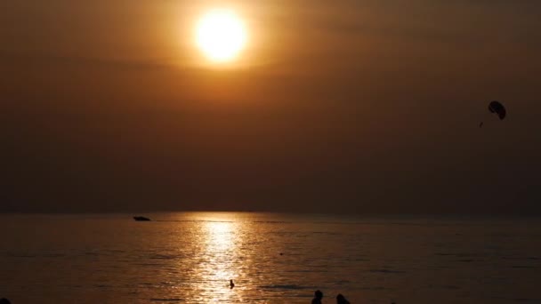 Κίνηση αλεξιπτωτιστών στην τροπική παραλία το ηλιοβασίλεμα. Ήρεμα θαλάσσια νερά και. παραλία με αλεξίπτωτο. Ρυμούλκηση με αλεξίπτωτο πίσω από μια βάρκα πάνω από τη θάλασσα. Σιλουέτα του αλεξιπτωτιστή ενάντια στη ρύθμιση — Αρχείο Βίντεο