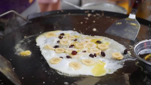 在夜市,在平底锅里煎鸡蛋,煎蛋,有香蕉和葡萄干。甜蜜的街头食品。4k — 图库视频影像