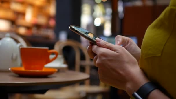 Primer plano de la mano de una mujer usando un teléfono inteligente mientras está sentada en la cafetería. Chica utiliza aplicaciones móviles. 4k — Vídeos de Stock
