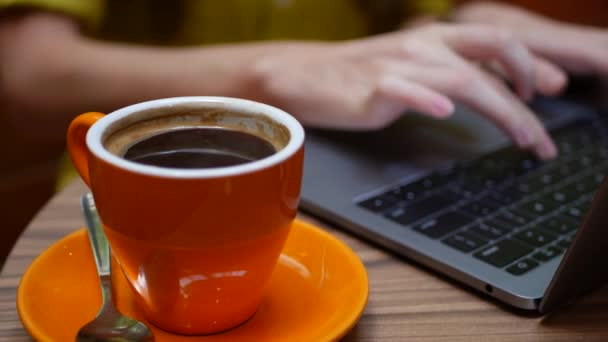 Mujer trabajando en un portátil con una taza de café en la mesa, trabajo distante de un café. Concepto de trabajo independiente. 4k — Vídeo de stock