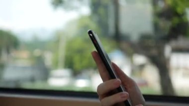 Kadın elleri cep telefonundan otobüse biniyor. Otobüs, arka planda geçen şehir ile pencere akıllı telefon kullanarak kadın closeup vurdu. E-postalar okuma. Mesaj mesajı. 4k