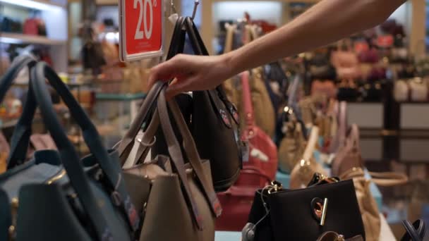 Молода жінка вибирає синтетичну шкіряну сумку в магазині одягу та аксесуарів. Клієнтська дівчина купує сумку на продаж в торговому центрі. Дисконтна концепція. 4-кілометровий — стокове відео