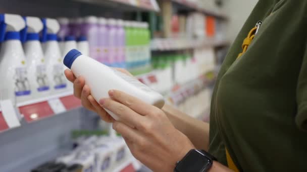 Mujer joven elige productos químicos domésticos en el supermercado. Lee la estructura de la etiqueta. Primer plano. 4k — Vídeo de stock