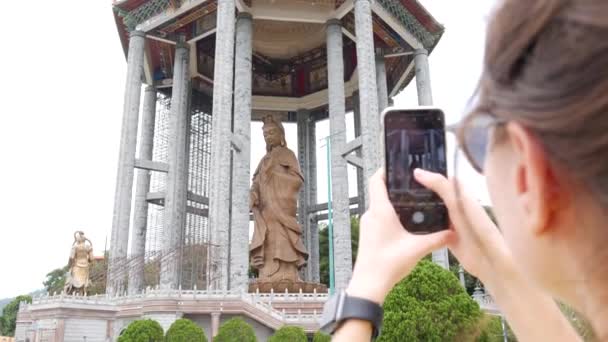 Mujer haciendo fotos por teléfono inteligente de la Diosa de la Misericordia Guanyin o Guan Yin estatua en templo budista. Visitar Complejo Espiritual y Cultural. 4k — Vídeos de Stock