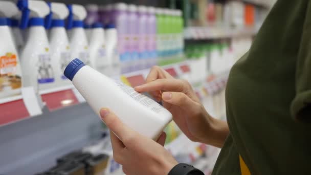 Mujer joven elige productos químicos domésticos en el supermercado. Lee la estructura de la etiqueta. Primer plano. 4k — Vídeos de Stock