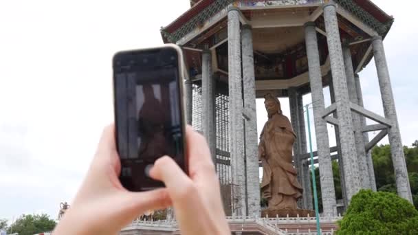 Mujer haciendo fotos por teléfono inteligente de la Diosa de la Misericordia Guanyin o Guan Yin estatua en templo budista. Visitar Complejo Espiritual y Cultural. 4k — Vídeos de Stock