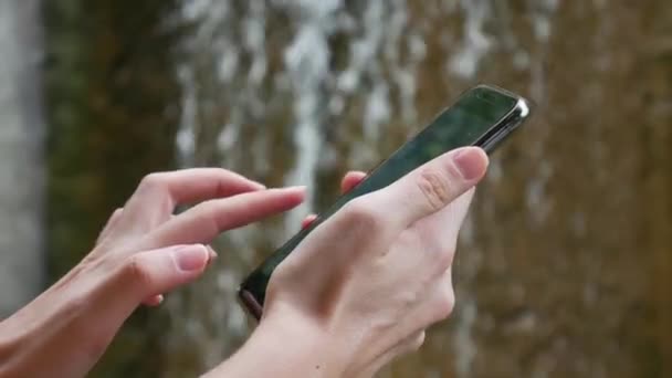 Kvinnan använder en smartphone i naturen på bakgrunden av vattenfall, beroende på Internet. Ekoturism koncept. Närbild. 4K — Stockvideo