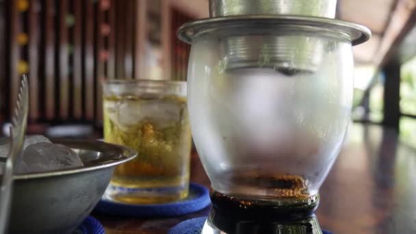 Elaboración de café negro utilizando un filtro de aleta tradicional vietnamita en la cafetería. El café gotea lentamente en una taza de vidrio. Ca phe den da. Primer plano. 4k — Vídeo de stock